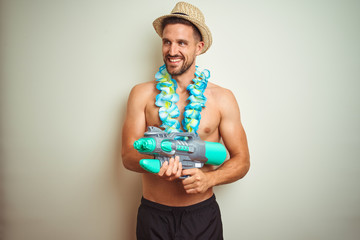 Handsome shirtless man wearing hawaiian lei and water gun over background with a happy face standing and smiling with a confident smile showing teeth