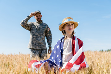 Poster - selective focus of cheerful kid standing with american flag near soldier