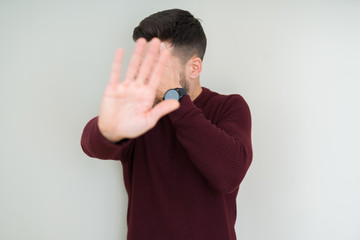 Sticker - Young handsome man wearing a sweater over isolated background covering eyes with hands and doing stop gesture with sad and fear expression. Embarrassed and negative concept.