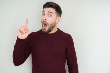 Young handsome man wearing a sweater over isolated background pointing finger up with successful idea. Exited and happy. Number one.