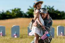Military Father In Uniform Hugging Child Near Headstones In Graveyard