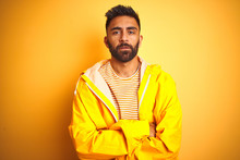 Young Indian Man Wearing Raincoat Standing Over Isolated Yellow Background Skeptic And Nervous, Disapproving Expression On Face With Crossed Arms. Negative Person.