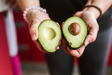 Unrecognizable Female Demonstrating Two Halves Of Ripe Avocado To Camera While Standing On Blurred Background On Kitchen