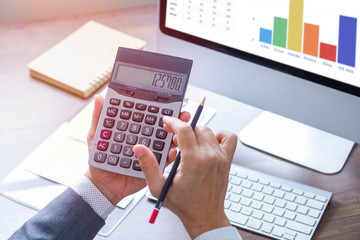 Wall Mural - Businessman using calculator reviewing a financial statements and reports for business performance and a return on investment or investment risk analysis.