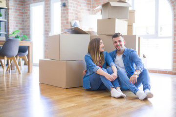 Poster - Young beautiful couple in love moving to new home, sitting on the floor very happy and cheerful for new apartment around cardboard boxes