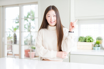 Beautiful Asian woman wearing casual sweater with a big smile on face, pointing with hand and finger to the side looking at the camera.