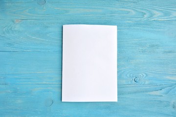 Wall Mural - Blank sheet of white paper for design banner or card on textured blue background, selective focus. Clear page with empty space for image or text on wooden turquoise backdrop. Mockup concept 