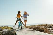 Two Women Having Fun With A Bicycle At Beach