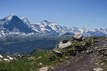 Hiking Trail Sign (white Red White Stripes) On A Rock Next To Hiking Trail With Mountains (eiger, Moench And Jungfrau) In The Background.
