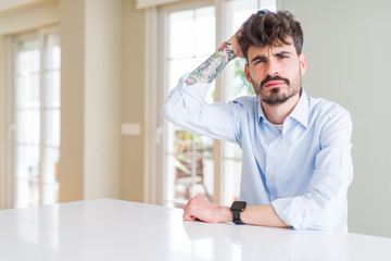 Wall Mural - Young businesss man sitting on white table confuse and wonder about question. Uncertain with doubt, thinking with hand on head. Pensive concept.