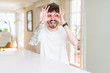 © Krakenimages.com - Young man wearing casual t-shirt sitting on white table doing ok gesture like binoculars sticking tongue out, eyes looking through fingers. Crazy expression.