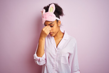 Sticker - Young african american woman wearing pajama and mask over isolated pink background tired rubbing nose and eyes feeling fatigue and headache. Stress and frustration concept.