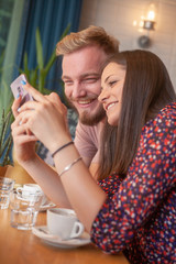 two friends sitting together, smiling while looking at a phone screen together.