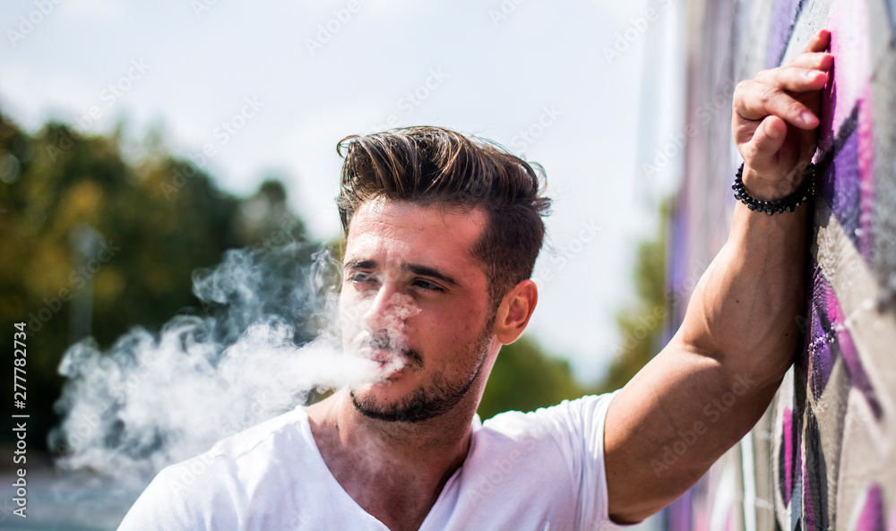 handsome man smoking cigarette Handsome man smoking e-cigarette, vaping outdoor in city setting Stock  Photo