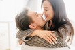 Close-up portrait of kissing couple spending morning together. Indoor photo of blissful european girl with long black hair hugging with husband on light background.