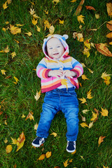 Wall Mural - Girl sitting on the grass and playing with colorful autumn leaves