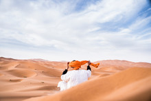 Rear View Of Man Wearing Turban While Sitting On Sand Dune In Desert