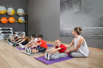 Wall Mural - Trainer helping children to do physical exercise in school gym. Healthy lifestyle