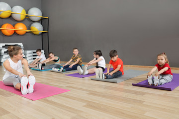 Wall Mural - Cute little children and trainer doing physical exercise in school gym. Healthy lifestyle