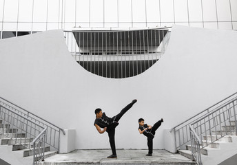 Father and son are engaged in Wushu in the city. The photo illustrates a healthy lifestyle and sport. The father trains the son.