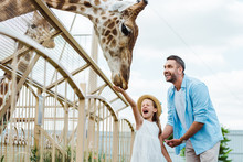 Selective Focus Of Cheerful Man And Kid With Closed Eyes Feeding Giraffe In Zoo
