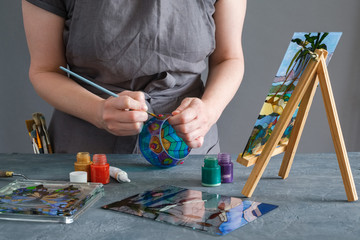 Painter holding a paintbrush in his hand and painting with stained glass paints on a glass vase.