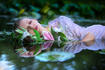 Beautiful sexy woman lying in the water in a white dress with a bouquet of lilies.