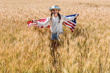 Wall Mural - happy kid in straw hat holding american flag in golden field