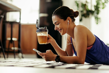 Happy woman texting on the phone while drinking smoothie at home.