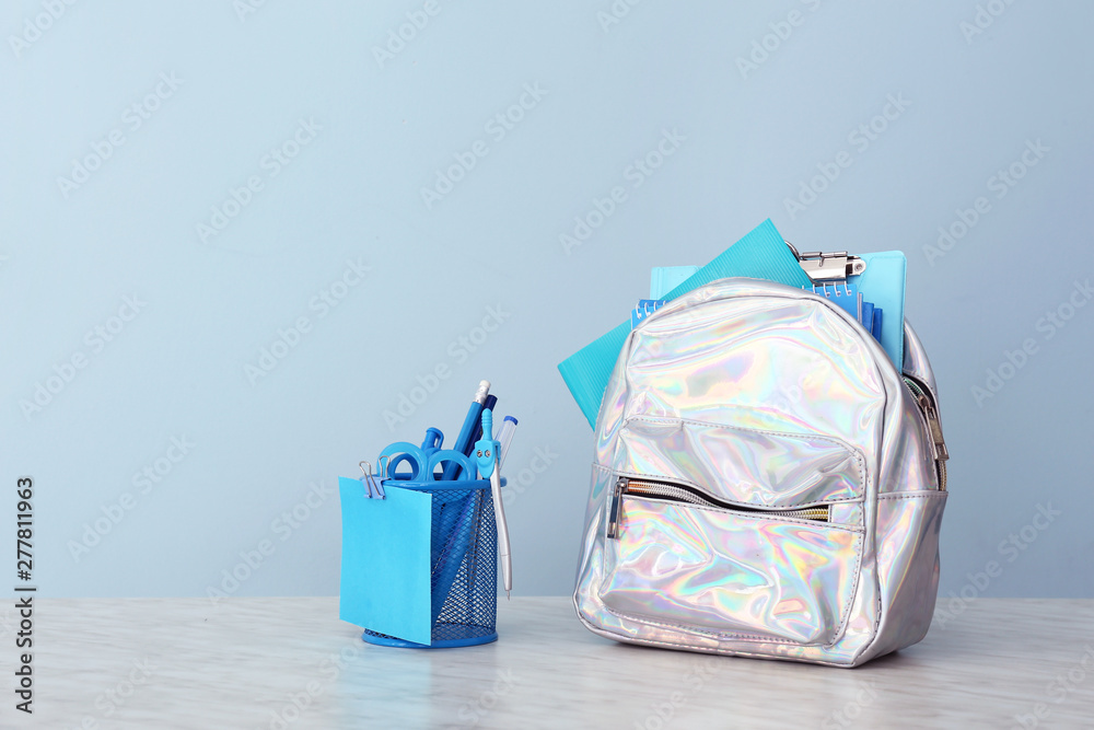 School backpack and stationery on table against color background
