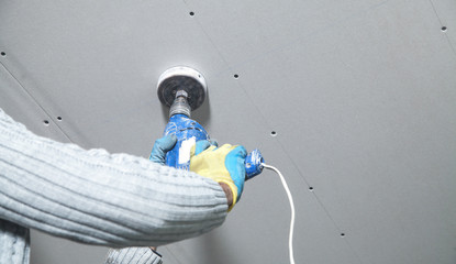 Wall Mural - Worker holding a power drill. Make a hole in the ceiling. Install lamp