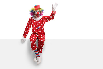 Funny clown sitting on a white panel and waving