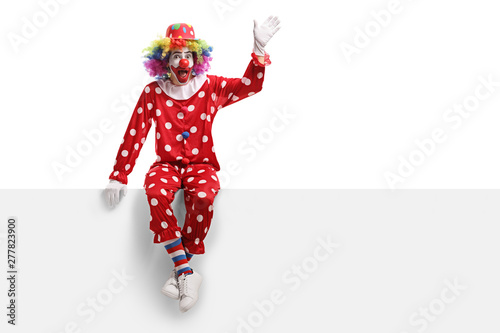 Fotografía Funny clown sitting on a white panel and waving