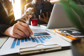 Businessman hand using laptop and tablet with social network diagram and two colleagues discussing data on desk as concept in morning light.