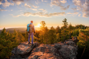 Hiker with backpack standing on a rock and enjoying sunset on mauntain