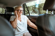 © rh2010 - Senior business woman talking with phone while sitting on the back seat in the modern car. Concept of a business life on retirement