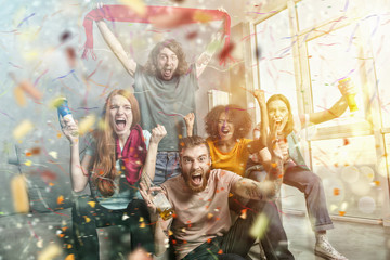 Happy friends of football fans watching soccer on tv and celebrating victory with falling confetti.