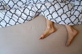 Fototapeta Dmuchawce - Natural female feet in bed with patterned bed sheet.