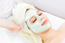 Portrait Of Beautiful Woman Laying With Towel On The Head. Young Girl Enjoys Green Cream Facial Mask. Lady Getting Spa Treatment At Beauty Salon.
