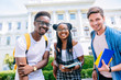 © Iryna - Low angle view of three positive defferent races friends students on university campus in autumn time.