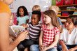 © Monkey Business - Group Of Elementary School Pupils Sitting On Floor Listening To Female Teacher Read Story