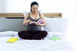© Watcharin - The pregnant woman sitting on bed,reading book with smile and happy feeling,blurry light around