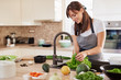 © nenadaksic - Cheerful attractive Caucasian woman in apron washing salad in kitchen. Dinner at home concept.