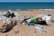 Dirty sea shore. Garbage on the sandy beach with waves on background. Environment pollution. Ecological problem.