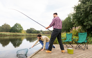 leisure and people concept - male friends with net and fishing rods on lake pier