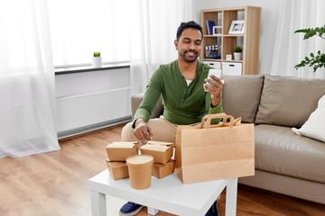 Wall Mural - communication, leisure and people concept - indian man using smartphone for takeaway food order check up at home