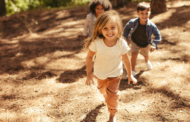 Poster - Cute girl running up hill in a park with friends