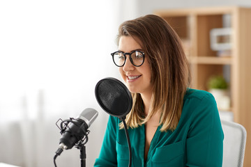 Wall Mural - technology, mass media and people concept - woman in glasses with microphone talking and recording podcast at studio