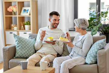 Sticker - family, generation and people concept - happy smiling senior mother and adult son eating cake with coffee at home