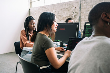 Confident female and male IT professionals sitting in board room during meeting at creative workplace